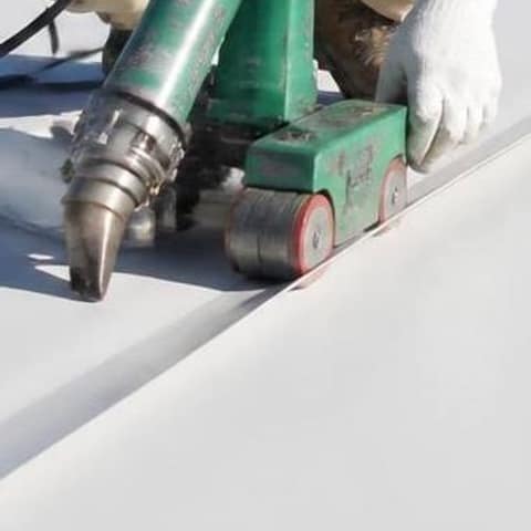 Soldadora de aire caliente y rodillo sellando una costura en una membrana de techo